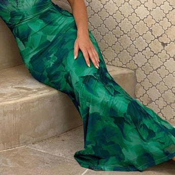 Green floral satin maxi dress with open back design, featuring a flowing skirt and sleeveless style, suitable for summer occasions.