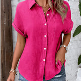 A woman wearing a pink rose short sleeve cotton blouse with pleated back detail, visible from the shoulders down to the arms.