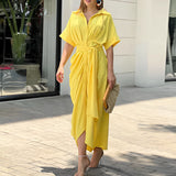Green and white abstract print V-neck wrap midi dress with short sleeves, modeled by a woman standing. The dress is in a yellow 2XL variant, suitable for summer fashion and formal wear occasions.