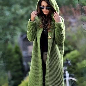 
A woman wearing a green oversized hooded cardigan made from chunky knit material. She has sunglasses resting on her head and the cardigan features long sleeves and a comfortable fit, ideal for layering in cooler weather.