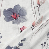 A grey linen blouse featuring a delicate botanical pattern with pink floral designs on the fabric, showcasing an artistic arrangement of flowers, petals, and branches.