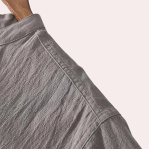 A grey linen button-up shirt with a collar, displayed on a wooden surface, highlighting its breathable and sustainable fabric, suitable for summer fashion.