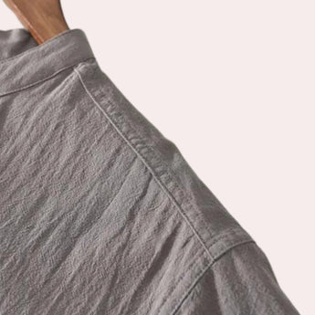 A grey linen button-up shirt with a collar, displayed on a wooden surface, highlighting its breathable and sustainable fabric, suitable for summer fashion.