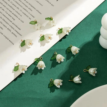 Handmade porcelain earrings featuring delicate white blossom flowers and green leaf details displayed on a natural green background.