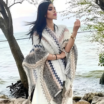 Handmade woolen bohemian poncho in white, featuring a colorful winter fashion design; model wearing the poncho outdoors showcasing its stylish sleeves and drape, with a clear sky in the background.