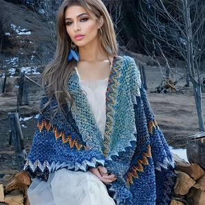 A fashion model wearing a handmade woolen bohemian poncho in a blue color, showcasing a colorful winter fashion piece. The poncho features a cozy and stylish design suitable for cool weather, with detailed textile patterns and a one-size-fit. The image captures the shoulder, neck, and sleeve areas, highlighting the fashion-forward design in flash photography.
