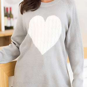 
A woman wearing a grey oversized sweater featuring a heart pattern, styled as a cozy knit pullover.