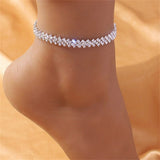 A silver-tone zigzag anklet featuring a heart-shaped diamond, elegantly worn on a bride's ankle, highlighting intricate design and sparkling jewelry perfect for weddings.