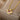 A hand holding a diamond-encrusted heart-shaped pink gemstone gold necklace against a beige wooden background.