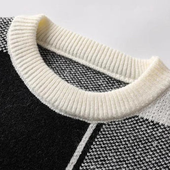 Herringbone Knit Sweater in Black & White displayed on a table with a subtle winter fashion pattern.