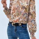 High-neck paisley blouse in a bohemian style, featuring a white fabric with intricate patterns, long sleeves, and a stylish autumn design. The blouse is worn by a model with shoulder-length hair, showcasing the fashionable and elegant look of the top.