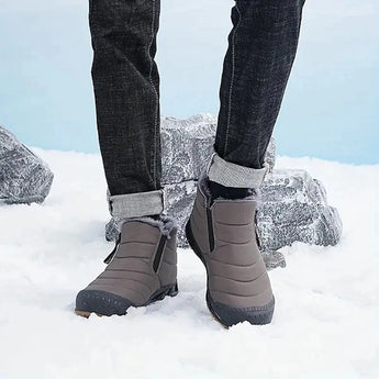A pair of high-traction anti-slip rubber sole athletic sneakers worn by a person standing in a snowy outdoor setting, with visible denim pants and legs bent at the knee.