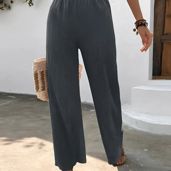 Woman wearing high-waisted pleated pink trousers, standing with hands in pockets, showcasing lightweight summer fabric and tailored fit around waist, thighs, and knees.