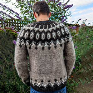 Icelandic wool sweater with a Nordic pattern, featuring a unisex design, displayed outdoors with grass and sky in the background. The sweater showcases long sleeves and a high neck in a vibrant purple hue.