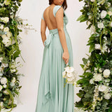 Ivory backless crossover strap bridesmaid maxi dress with pockets, featuring a flowing design and delicate shoulder straps, surrounded by natural greenery in an outdoor setting.