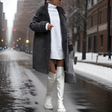 Ivory faux shearling winter coat with a double-breasted design, showcasing an oversized fit. The coat is worn standing in a snowy setting, highlighting its long sleeves and waist-length style.