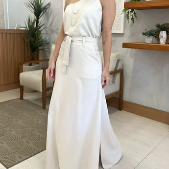 Ivory one-shoulder midi dress with an elegant slit, featuring a fitted silhouette, perfect for summer weddings and formal events, worn by a model with an updo hairstyle, surrounded by lush houseplants.