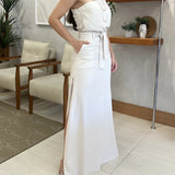 Ivory one-shoulder midi dress with an elegant design featuring a slit, suitable for summer and formal occasions, shown on a model with houseplant in the background.