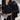Ivory women's cropped quilted puffer jacket with contrast piping in black, featuring a stylish design with a collar, long sleeves, and a fitted waist, modeled by a person with black hair.