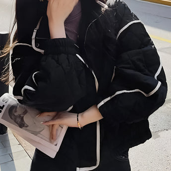 Ivory women's cropped quilted puffer jacket with contrast piping in black, featuring a stylish design with a collar, long sleeves, and a fitted waist, modeled by a person with black hair.