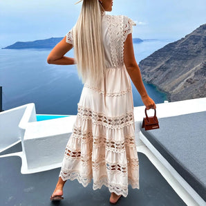 Lace tiered maxi dress in white with boho crochet details, featuring short sleeves and a fitted waist, worn outdoors with a bright, clear sky in the background.