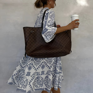 
A woman wearing a white dress holding a large brown oversized tote bag on her shoulder.