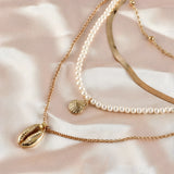 Layered gold necklaces with a pearl chain and seashell pendant, minimalist jewelry design.