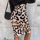Woman wearing a leopard print high-waist midi skirt paired with a black top, standing with one arm resting on her hip.