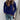A woman wearing a light beige ribbed knit sweater paired with blue jeans. The sweater features a casual chic design with long sleeves and a relaxed fit, highlighting the ribbed texture. The image showcases the shoulder and neckline details of the sweater, set against a neutral background.