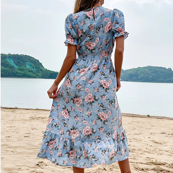 Light blue floral midi dress with V-neck and short sleeves, perfect for summer beachwear, modeled outdoors with a clear sky and water in the background.