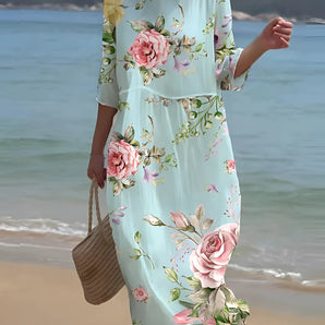 Light blue floral midi dress with sleeves, featuring a pastel beachwear design, displayed on a mannequin or model. The dress has a floral pattern and is styled with a focus on the neckline and shoulder area. The garment is a one-piece outfit suitable for casual beach outings.