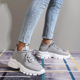 Light grey women's fashion sneakers with breathable mesh and cushioned sole, shown on a person’s feet.