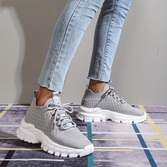 Light grey women's fashion sneakers with breathable mesh and cushioned sole, shown on a person’s feet.