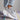Light grey women's fashion sneakers made of breathable mesh with a cushioned sole, displayed on a model's foot.