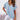Woman wearing a light pink V-neck blouse with short sleeves, standing with her hands on her hips.