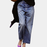 Light-wash high-waist denim jeans in faded blue, featuring a classic five-pocket design, worn by a person standing with hands near the waist, showcasing the thigh and knee areas.