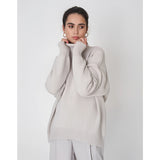 A light gray chunky knit turtleneck sweater featuring a cozy and warm design, suitable for winter fashion. The sweater has a thick collar, long sleeves, and is worn by a model.