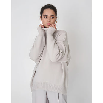 A light gray chunky knit turtleneck sweater featuring a cozy and warm design, suitable for winter fashion. The sweater has a thick collar, long sleeves, and is worn by a model.