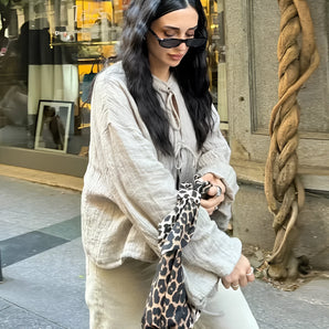 
A woman wearing a linen blouse paired with cream pants, accessorized with stylish sunglasses, showcasing an urban chic street fashion outfit.