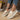 A pair of beige linen women's sneakers displayed outdoors, showcasing their eco-friendly and breathable design. The image features the sneakers on a human leg, emphasizing their casual fashion appeal, with a yellow dress and a flowerpot with greenery in the background.