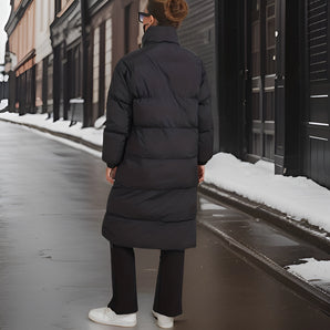 Women's long black insulated winter down coat with a stylish urban design, featuring a sleek overcoat style with a waist tie and knee-length hem, perfect for cold snowy weather.