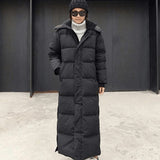 Woman wearing an oversized, full-length black puffer coat with quilted design, standing outdoors.