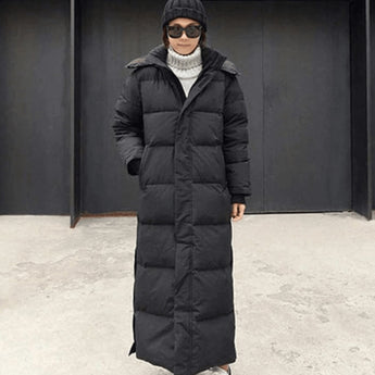 Woman wearing an oversized, full-length black puffer coat with quilted design, standing outdoors.