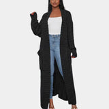 
A woman wearing a long black ribbed oversized knit cardigan, suitable for winter wear, featuring a collar and long sleeves, paired with a bag over her shoulder.
