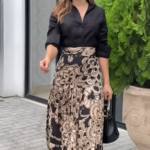 
A woman is wearing a stylish outfit suitable for the office, featuring a long paisley skirt paired with a black blouse.
