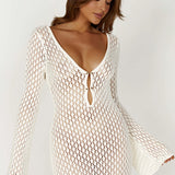 Long sleeve white crochet midi dress, styled as a bohemian beach cover-up, highlighting its intricate crochet pattern and flowing fit.