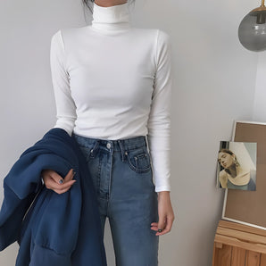A woman wearing a long sleeve white slim fit turtleneck, styled as a fall fashion top, with a close-fitting design that highlights her shoulders and arms. She is accessorized with sunglasses, adding a chic touch to the outfit. The top is in a 2XL size.