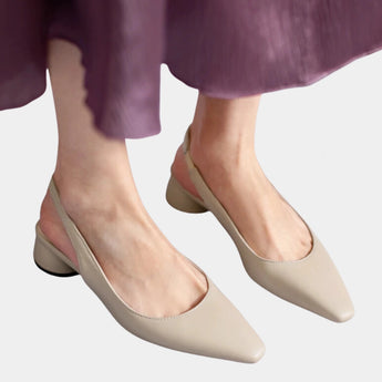 Black leather women's low-heel minimalist flats being worn, showcasing comfort and style with a focus on the foot and leg positioning against a floor background.