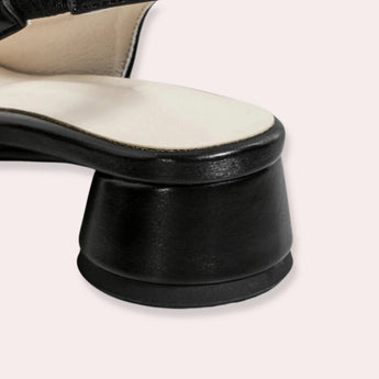 Women's minimalist black leather low-heel flats placed on a textured surface, highlighting their sleek design and comfort-focused construction.
