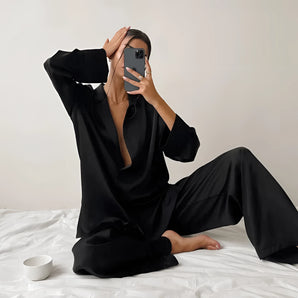 Luxurious designer black silk pajama set featuring a chic loungewear design, modeled by a person wearing sunglasses. The set includes long sleeves and offers a comfortable and stylish fit, captured in flash photography.
